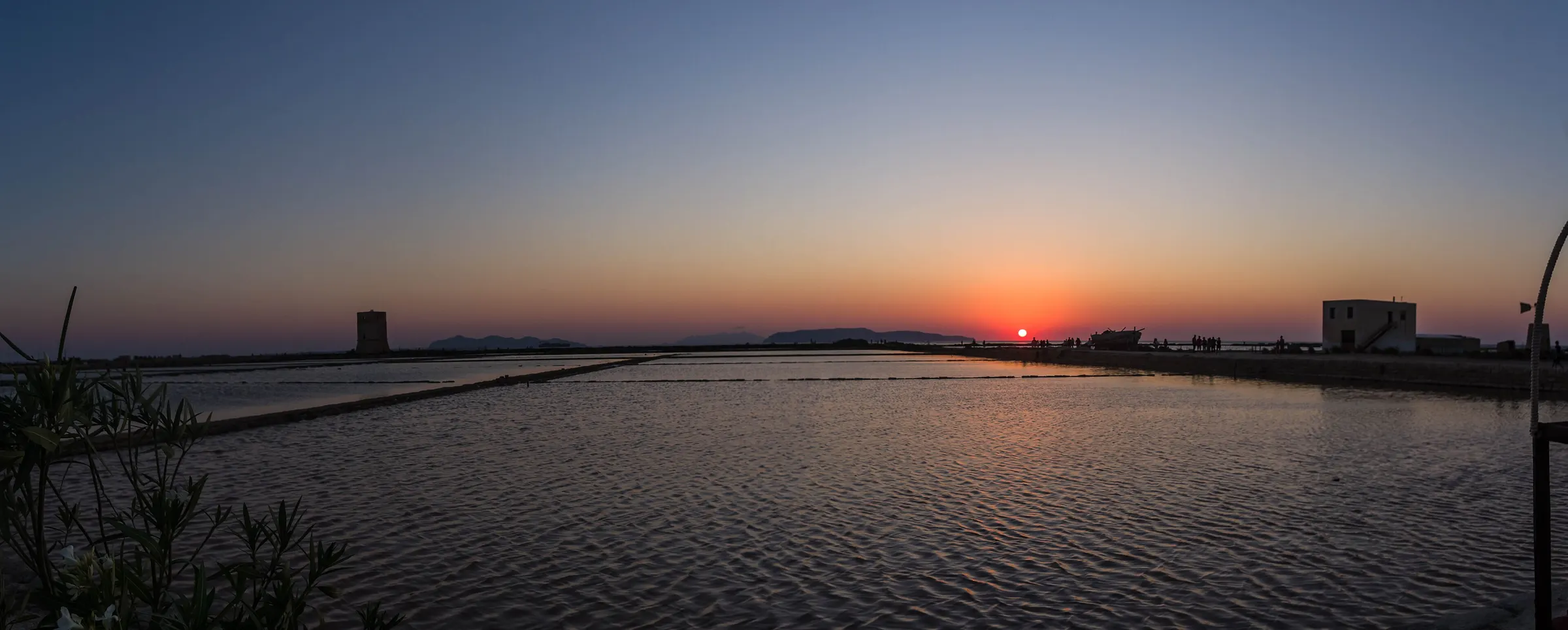 Sunset over the flat basins of the Nubia salt pans, with a stone tower and a salt works dark against the horizon