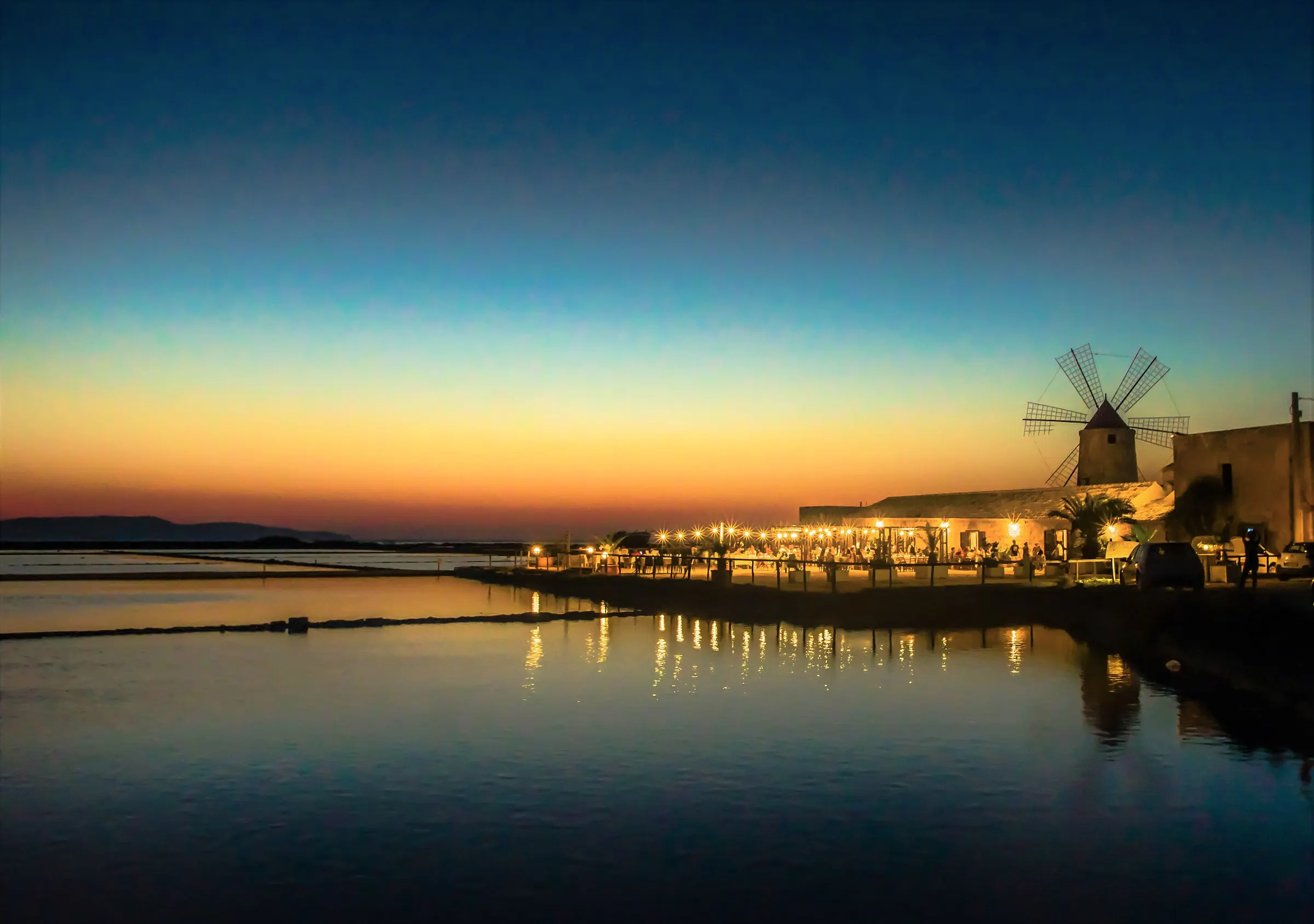 The windmill of the salt museum at Nubia at dusk, the lights of the buildings beside it reflected in the still basin