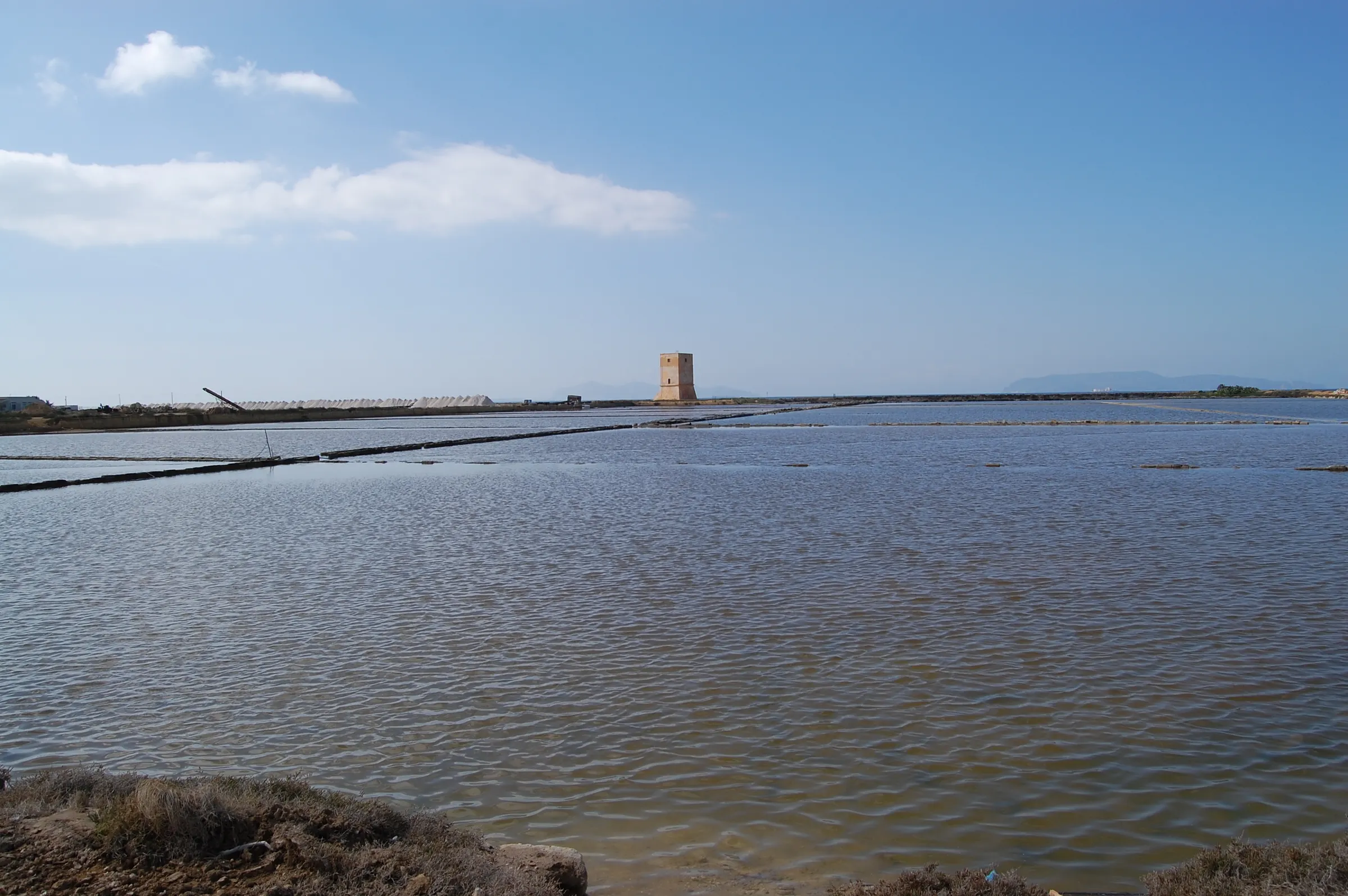 A wide, shallow salt basin under a blue sky, with the square Nubia tower standing on the far bank