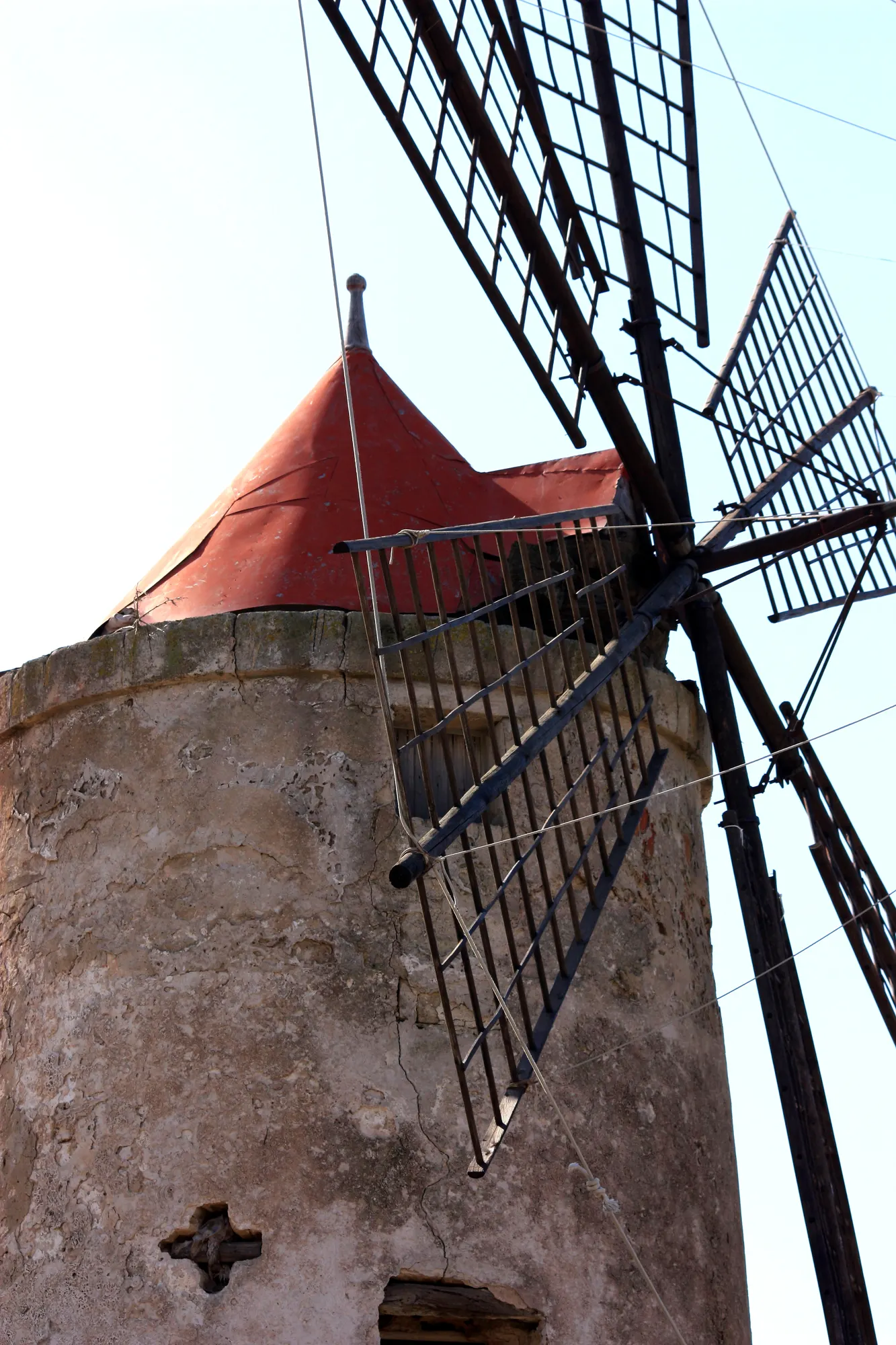 A salt-pan windmill seen from below, its round stone tower and red conical cap behind the wooden sails