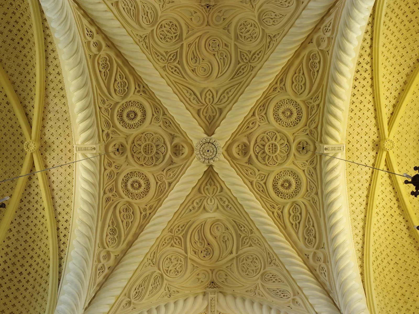 An ornate carved ceiling in pale stone, its ribbed vaults covered with rosettes and tracery
