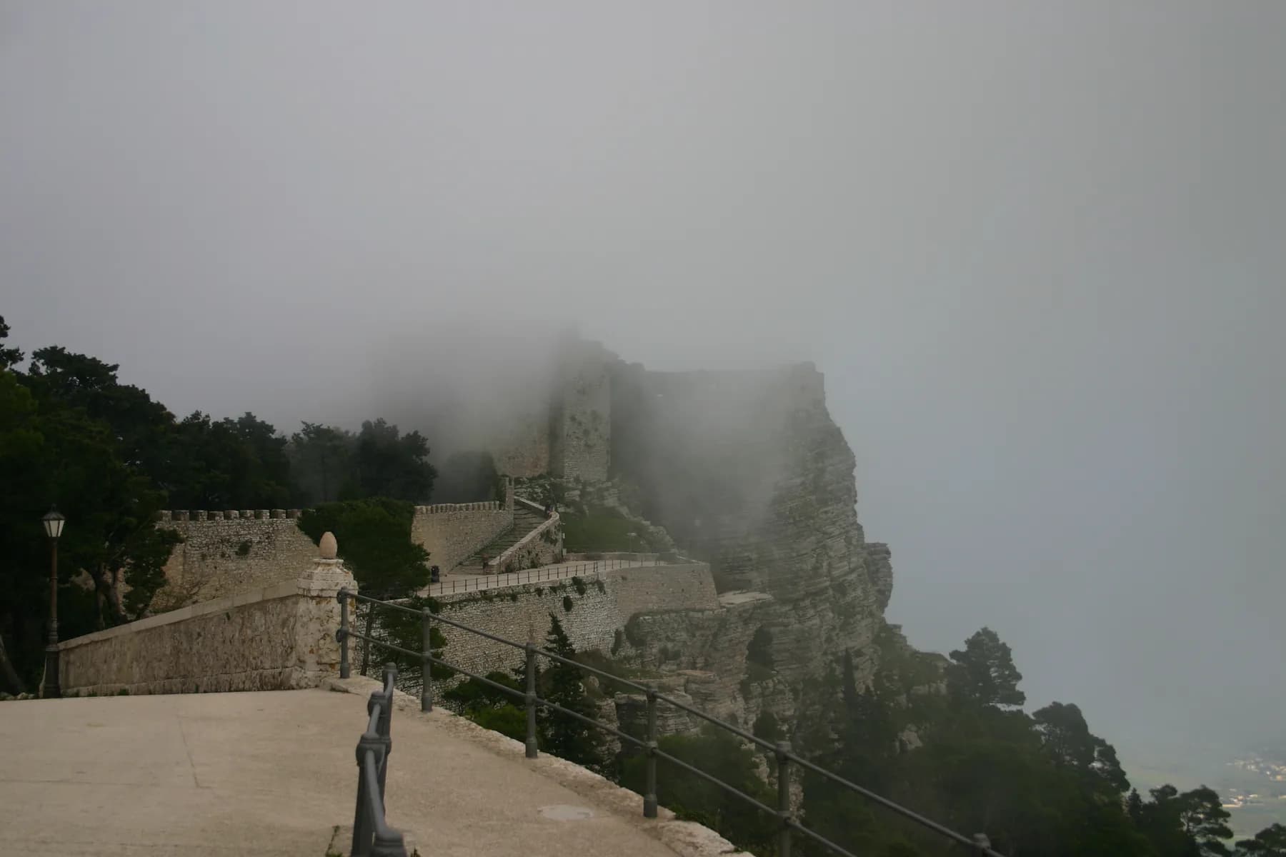 Cloud rolling over the castle walls and the cliff edge, with a lamp post and a walled terrace in the foreground