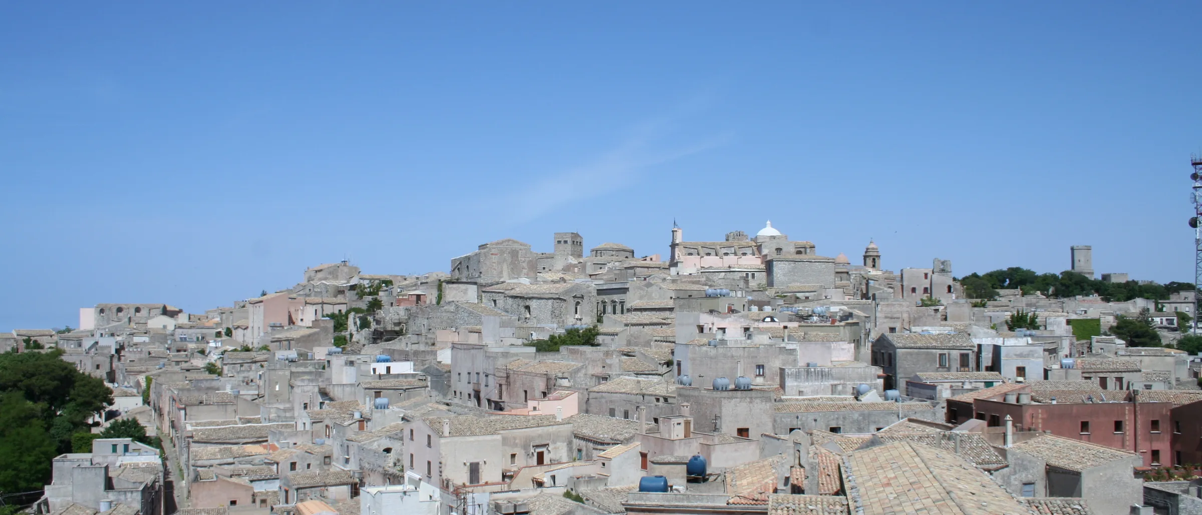 The pale stone houses and church towers of Erice spread across the top of the mountain under a clear sky