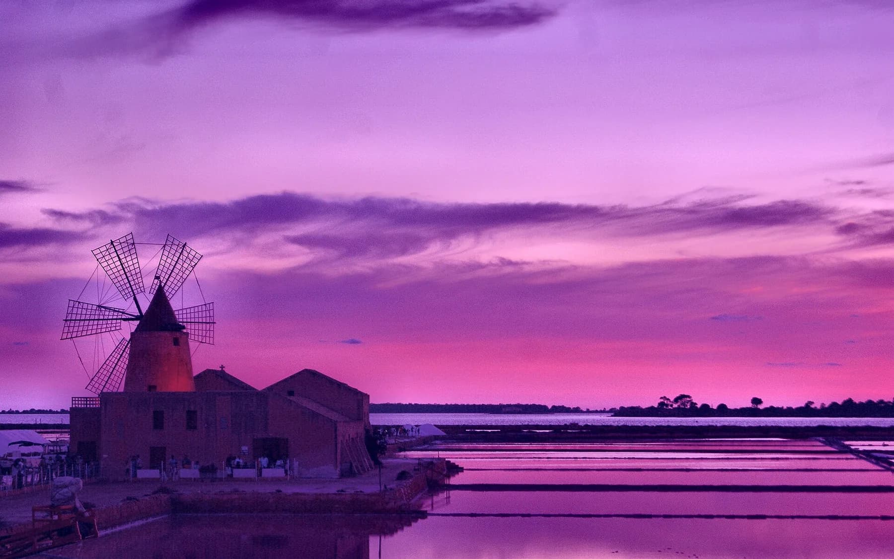 A windmill and a salt works silhouetted against a violet sunset, with the flooded pans reflecting the sky