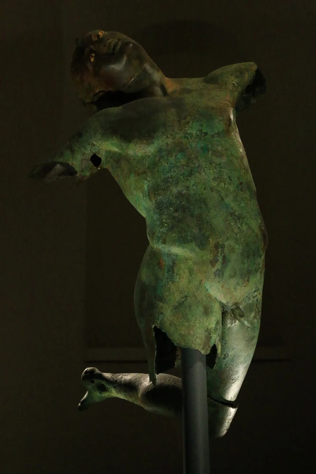 The bronze Dancing Satyr of Mazara del Vallo, its torso twisting in mid-leap, lit against a dark background