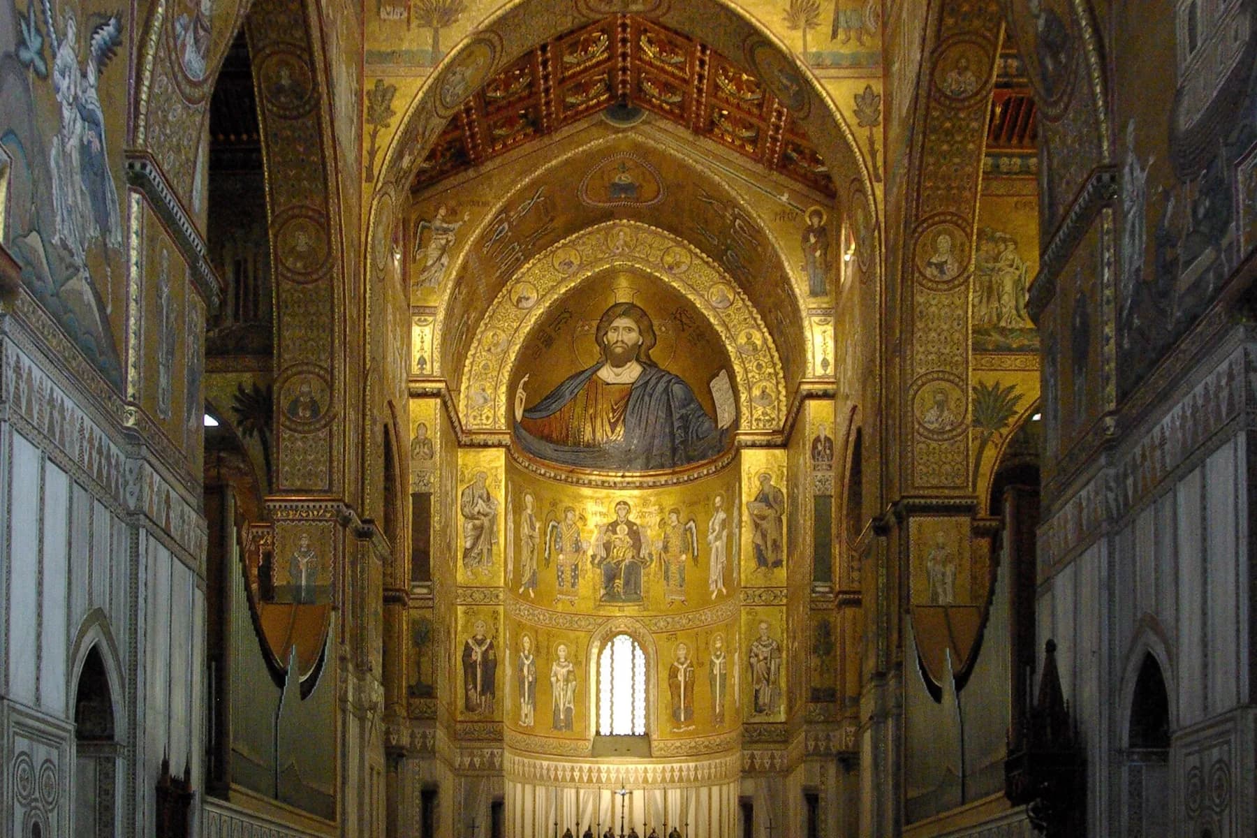 The interior of Monreale cathedral, its apse and arches entirely covered in gold ground mosaic with a large figure of Christ above the altar