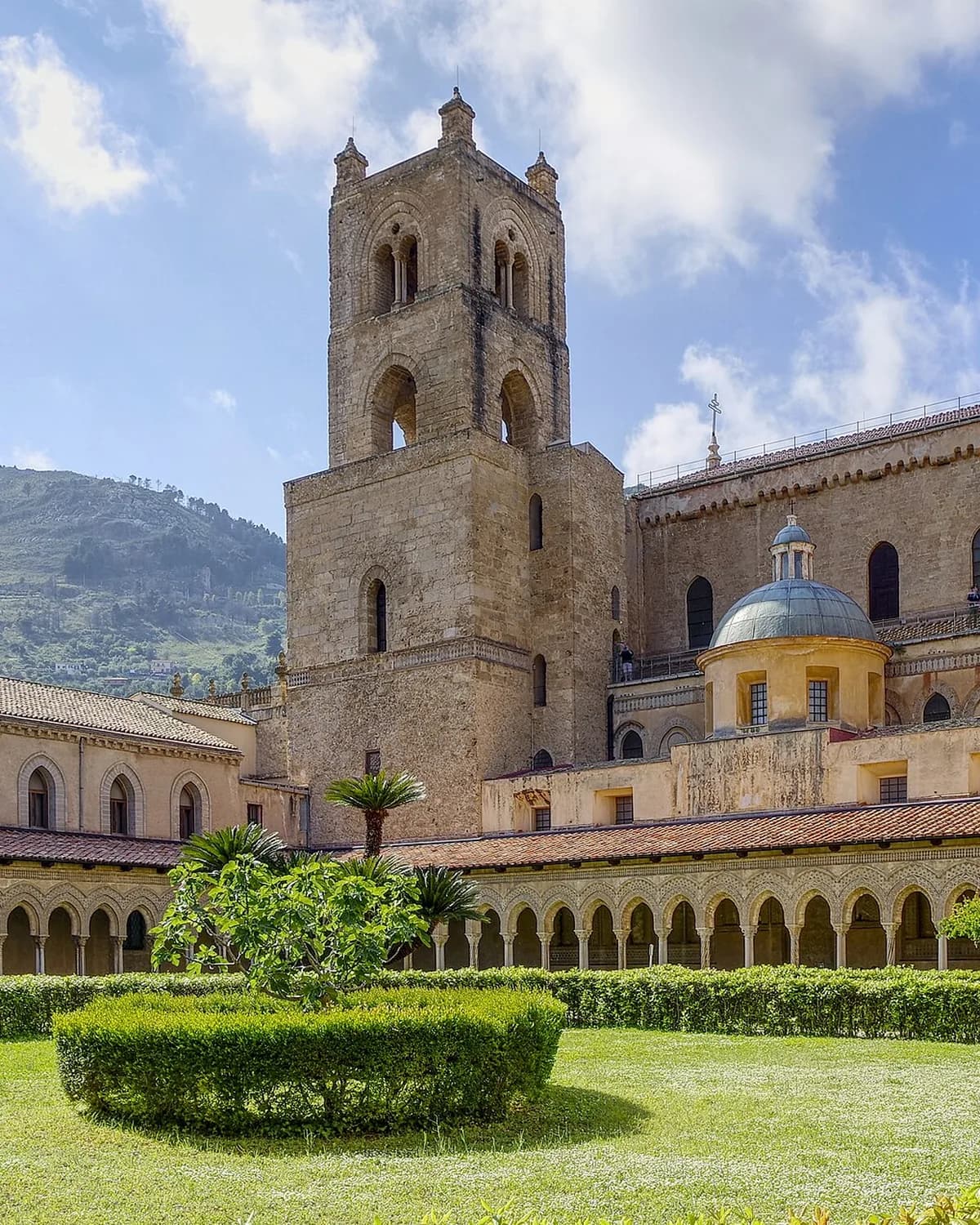 The cathedral bell tower and dome at Monreale seen from the cloister garden, with rows of small carved arches along the arcade below