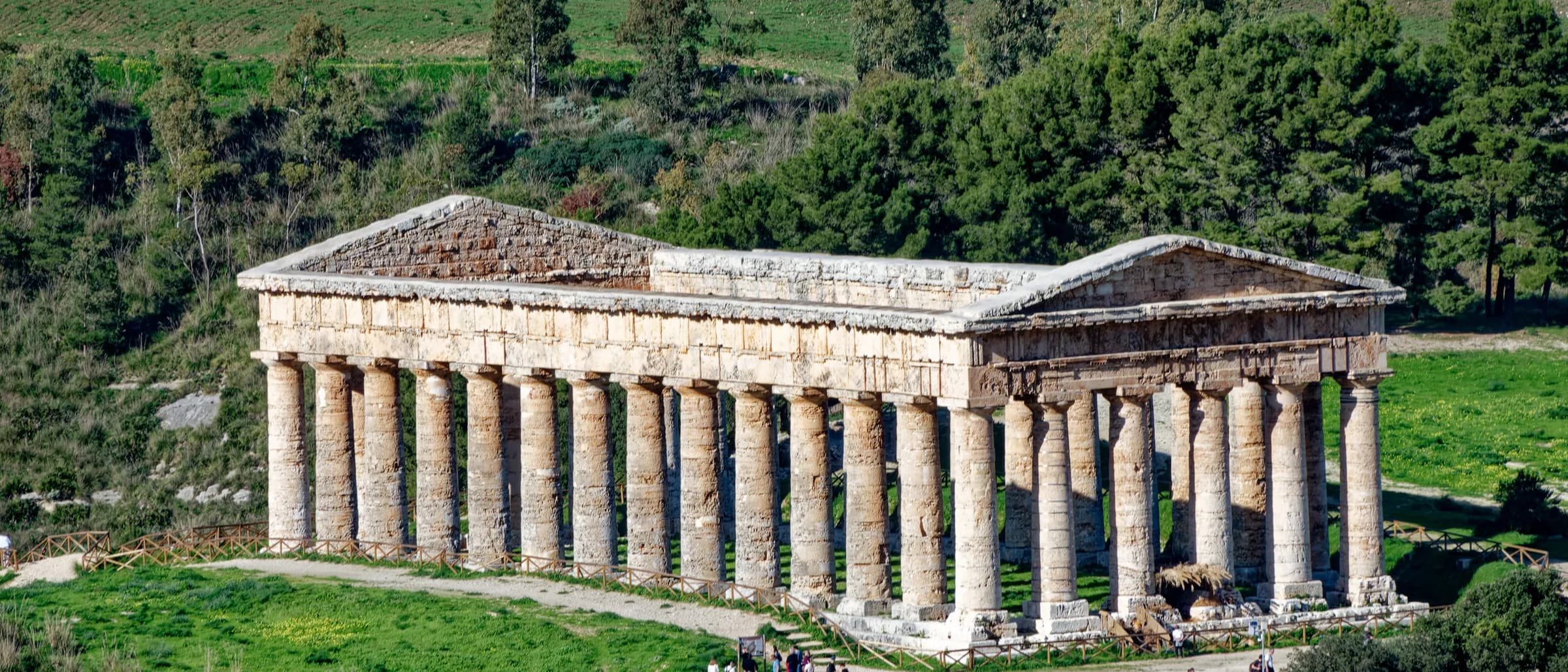 The Doric temple at Segesta seen from above, its colonnade complete and standing in open grassland with wooded hills behind