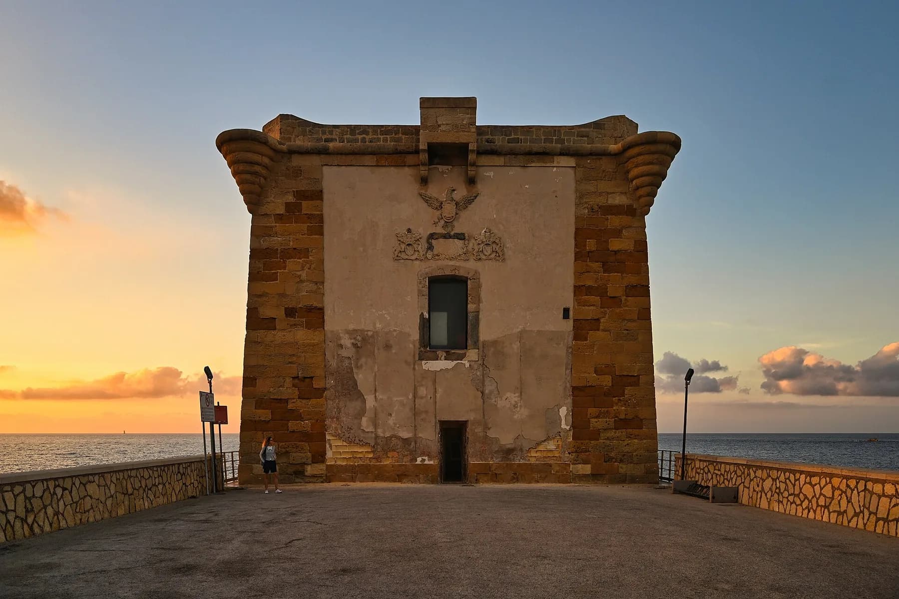 The Torre di Ligny in Trapani at sunset, seen from the paved terrace in front of it, with the sea on the horizon
